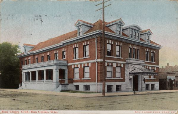 Colorized postcard of a red brick building on a corner of an intersection. The building has a porch and balcony on the side. Caption reads: "Eau Claire Club, Eau Claire, Wis."