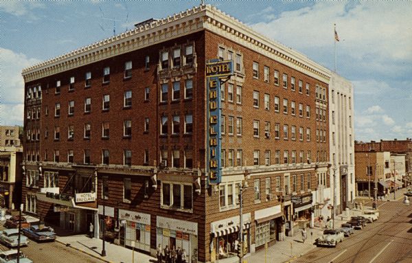 Elevated view of the Hotel Eau Claire and its three-story tall electric sign. The hotel is on a corner, and cars are parked along the curbs, and pedestrians are on the sidewalks.
