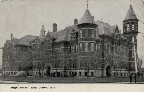 Corner view of the high school, a large brick building with turrets and gables. Students are standing on the sidewalk on the right, and also along the front of the building. Caption reads: "Hign School, Eau Claire, Wis."