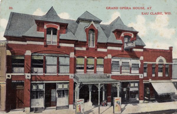 Colorized postcard with an elevated view of the Eau Claire Opera House, which has a roofed entrance over the sidewalk. At the curb are posters of coming attractions. Caption reads: "Grand Opera House, at Eau Claire, Wis."