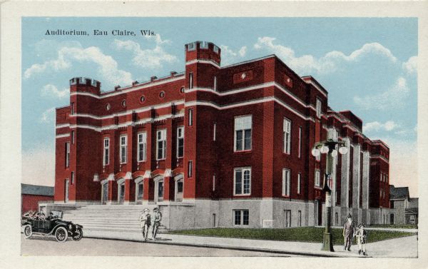 Colorized postcard of the Auditorium, a large red brick building with wide steps up to the entrance. A Model T is parked at the curb, and a few pedestrians are standing on the sidewalk. Caption reads: "Auditorium, Eau Claire, Wis."