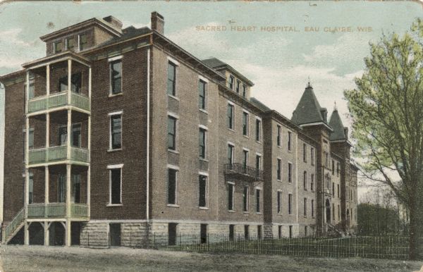 Colorized photographic postcard view of Sacred Heart Hospital. Balconies are on the second floor on the side of the building, and porches are on all three floors at the back.  Caption reads: "Sacred Heart Hospital, Eau Claire, Wis."