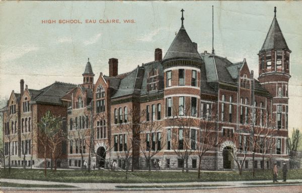 View from intersection towards the high school, a large brick building with turrets and arched entrances. Students are standing in front of the school, and on the sidewalk on the right. Caption reads: "High School, Eau Claire, Wis."