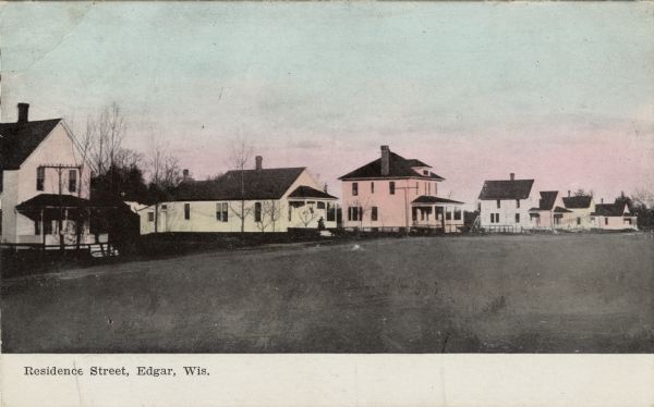 Colorized view of a row of wood frame houses. Caption reads: "Residence Street, Edgar, Wis."