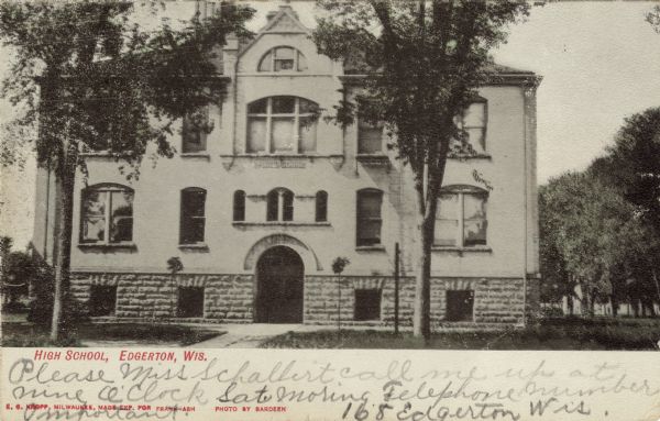 Black and white photographic postcard of the high school. A sign on the building reads: "Public School." Caption reads: "High School, Edgerton, Wis."