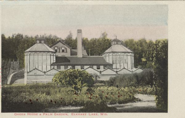 Colorized photographic view of a large glass greenhouse surrounded by trees. Caption reads: "Green House & Palm Garden, Elkhart Lake, Wis."