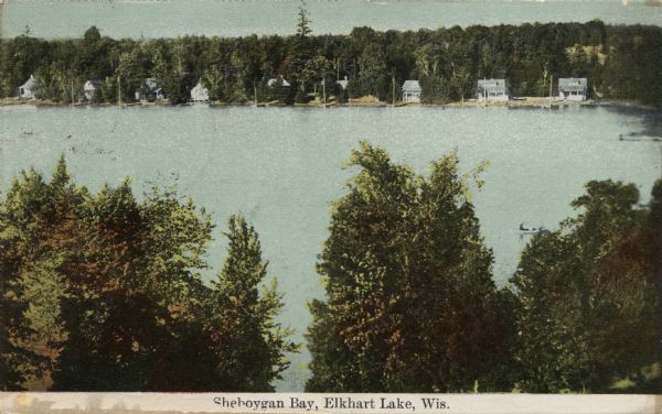 Elevated view over trees and Sheboygan Bay towards a row of lakeside dwellings. Caption reads: "Sheboygan Bay, Elkhart Lake, Wis."