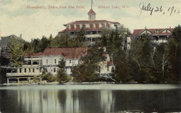 View of a large lakeside resort from the vantage point of Pine Point. Caption reads: "Bloomfield's, Taken from Pine Point, Elkhart Lake, Wis."