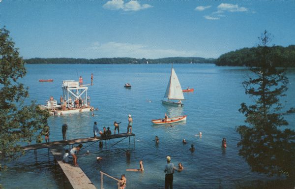 Elevated view towards dock, and a diving platform at Camp Brosius. A sailboat, rowboat and canoes are in the lake. Several people are swimming or standing on the pier. Text on reverse reads: "Camp Brosius on beautiful Elkhart Lake. A camp for boys and girls from 7 to 15 years of age. Owned and operated by Indiana University."