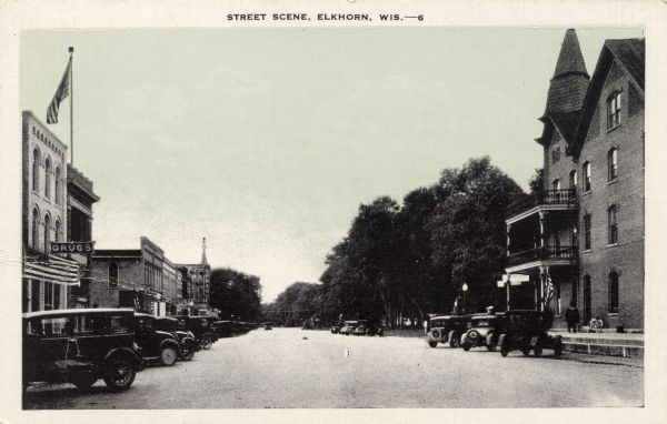 View down center of Walworth Street with the Sprague Theater on the left. A hotel is on the lower right. Automobiles are parked all along the street. Caption reads: "Street Scene, Elkhorn, Wis."