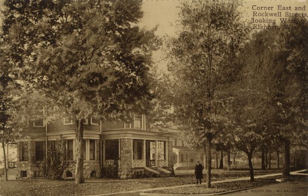 View from street of a residential neighborhood, showing houses with porches, trees along the street, and a man on the sidewalk. Caption reads: "Corner East and Rockwell Streets looking West, Elkhorn, Wis."