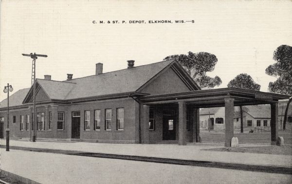 View across railroad tracks towards the depot with an empty platform. Caption reads: "C. M. and St. P. Depot, Elkhorn, Wis."