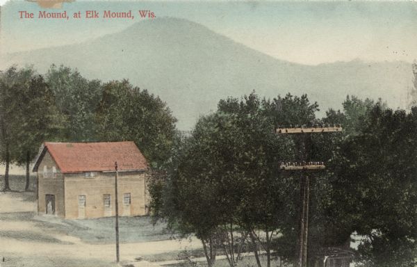 Colorized elevated view of a building standing amid trees. A hill is in the far background.