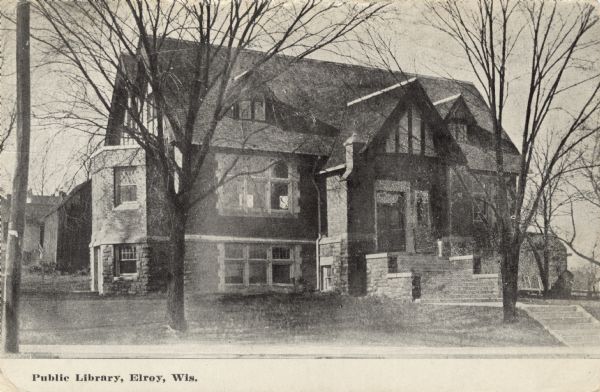 Black and white photographic postcard view of the public library with a gabled roof. Caption reads: "Public Library, Elroy, Wis."