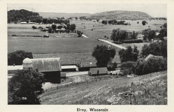 Elevated view from hill of a farm and the surrounding landscape. Hills are in the distance. Caption reads: "Elroy, Wis."