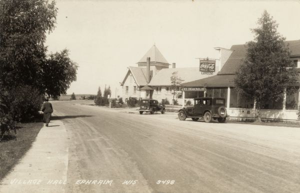 Wilson's Restaurant and the village hall. A woman is walking on the sidewalk on the left. Caption reads: "Village Hall, Ephraim, Wis."