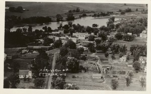 Aerial view of Ettrick. A river and fields are in the background. There is a church in the foreground on the left, and on the main street are commercial buildings, including a hardware store.