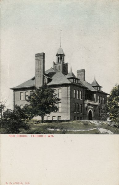 Corner view of the high school. There are chimneys on each side and a bell tower in the center. The bottom third of the postcard is blank. Caption reads: "High School, Fairchild, Wis."