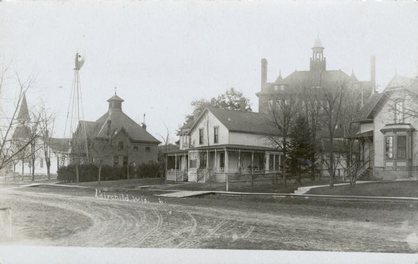A residential city block, with homes and a church. The high school is in the background. Caption reads: "Fairchild, Wis."