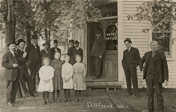 A group of men and four girls are standing in front of a hotel office. Penciled in on the reverse, some of the people are identified. Left to right: Billy Johnson, Wade Williams, G.T. Darby. Extreme right: Martin Irverson.