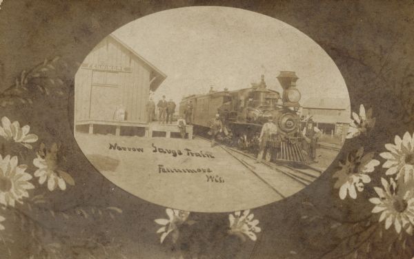 Sepia-toned oval-shaped photographic view of men posing with a narrow gauge train at the Fennimore Depot. Flowers surround the photograph. Caption reads: "Narrow Gauge Train, Fennimore, Wis."