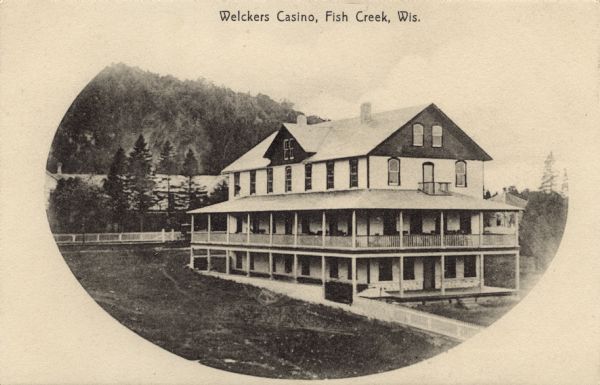 Slightly elevated view of a rectangular three-story building with wrap-around porches on the first and second floors. Tables and chairs are on the second floor porch. This is now the site of the Whistling Swan Inn. Caption reads: "Welckers Casino, Fish Creek, Wis."