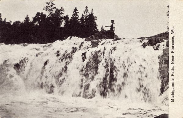 View of a waterfall with a man fishing from the top. Caption reads: "Michigamme Falls, Near Florence, Wis."