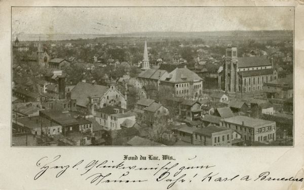 Elevated view of central Fond Du Lac. Lake Winnebago is in the distance. Churches and other buildings are in the foreground. Caption reads: "Fond du Lac, Wis."
