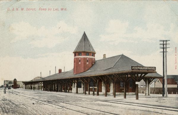 Hand-colored view looking across railroad tracks towards the Fond du Lac train station. One person is standing on the platform. Caption reads: "C. & N. W. Depot, Fond du Lac, Wis."