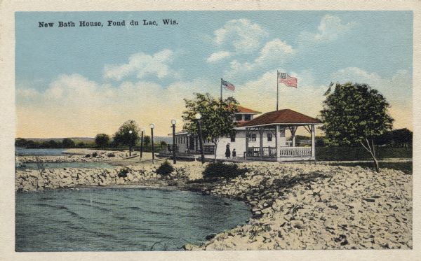 Color illustration of the bath house at the lake front, seen from along a stony shoreline. Caption reads: "New Bath House, Fond du Lac, Wis."