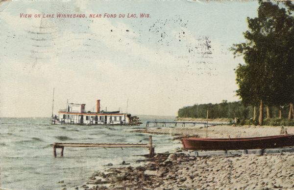 Scene at the lake front of Lake Winnebago. A steamer is on the lake, and a rowboat is pulled up on the shore near a pier. Caption reads: "View on Lake Winnebago, Fond du Lac, Wis."