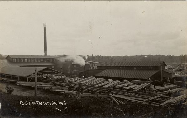 Elevated view of a lumber mill, with industrial buildings and stacks of lumber in the yard. Caption reads: "Mills at Fosterville, Wis."