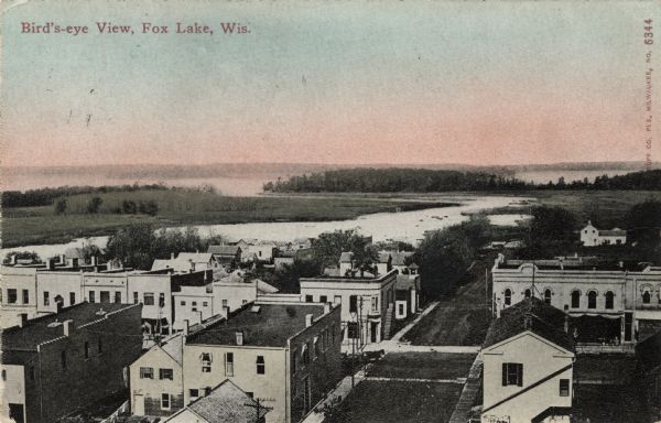 Bird's-eye view of downtown Fox Lake, with a marshy area and the lake in the background. Caption reads: "Bird's-eye View, Fox Lake, Wis."