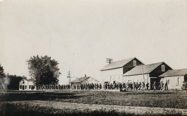 View across road and grass towards a group of soldiers marching through a Fox Lake neighborhood.