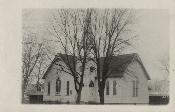 Exterior view of a white wooden church with arched stained-glass windows, bell tower and steeple. Caption reads: "Franksville, Wis."