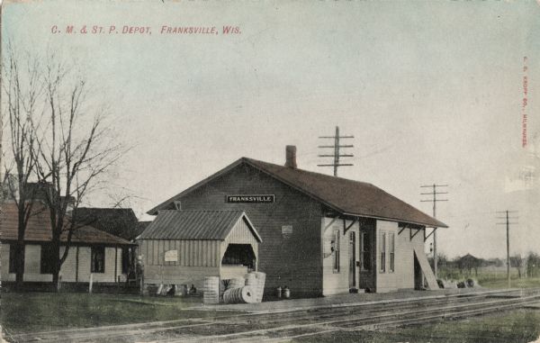 Hand-colored view of the Franksville Depot, a small wooden building next to the tracks. Caption reads: "C. M. & St. P. Depot, Franksville, Wis."