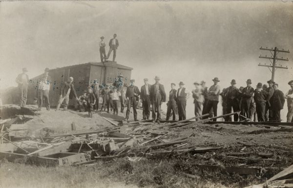 A group of men and boys are standing amid the wreckage of a train.