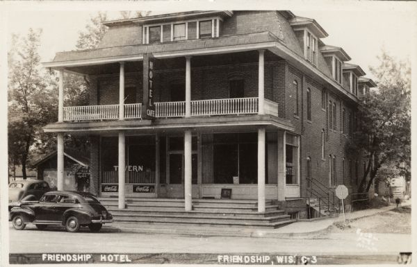 View across street towards the Friendship Hotel, including a tavern and cafe. Automobiles are parked in front. There are Coca-Cola signs under the front window.