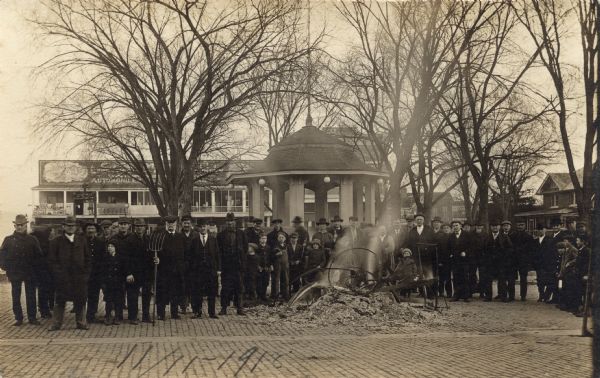 Crowd of men and young boys gathered around a smoldering pile of ash and scraps in the Galesville Town Square. The burned items were most likely German books and other materials burned in celebration of the end of World War I.