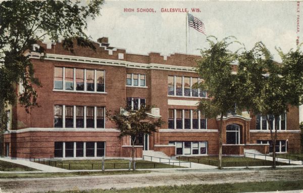 Hand-colored view of the high school. There is a flag flying from the roof.