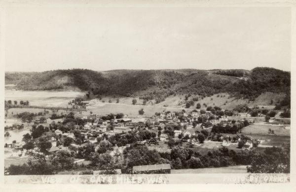 Elevated view of Gays Mills. A river is on the left, and there is a hill along the horizon. Caption reads: "View of Gays Mills, Wis."