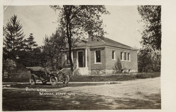 Black and white photographic postcard view of the exterior of the State Bank. A Model T is parked in the grass terrace in front of the bank. Caption reads: "State Bank, Genesee Depot, Wis."