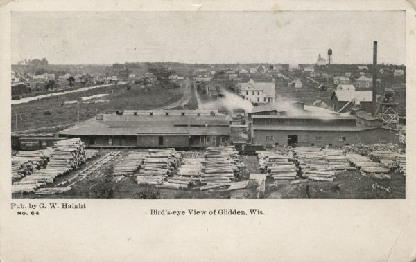 Elevated view of Glidden. The lumber mill is in the foreground. A church and a water tower are on the horizon.