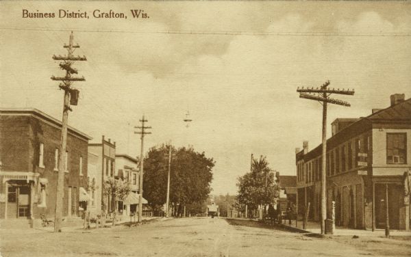 Street scene of the central business district. Shops and businesses are on both sides of the street. A horse and buggy is in the distance. Caption reads: "Business District, Grafton, Wis."