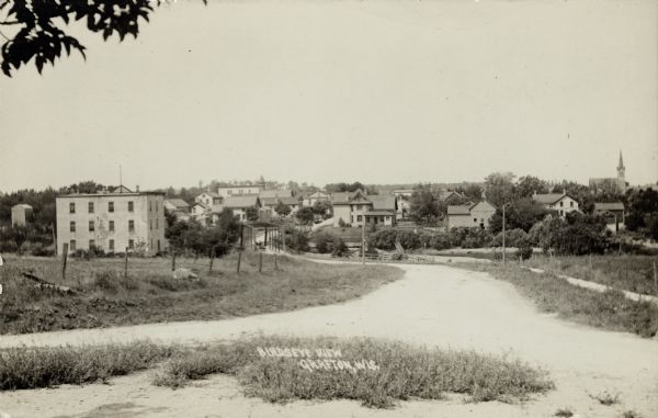 View of Grafton from the road leading into town. There is a bridge over the river, and a church is on the far right. Caption reads: "Birdseye [sic] View, Grafton, Wis."