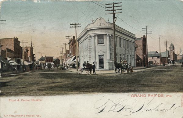 View of the intersection of Front and Center Streets. The First National Bank is on the corner. Horses and buggies are in the streets. Caption reads: "Front & Center Streets, Grand Rapids, Wis."