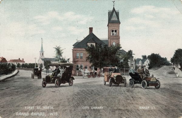View of an intersection in central Grand Rapids. Identified are: First Street on the left, the city library in the center, and Baker Street on the right. Automobiles and horses and buggies are in the street in the foreground. Caption at bottom reads: "Grand Rapids, Wis."