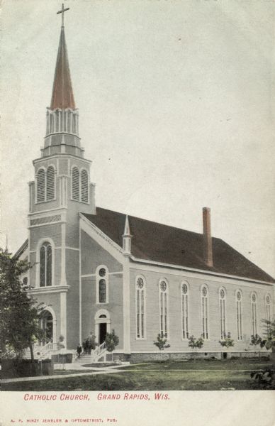 Three-quarter view of the Catholic Church. There is a steeple above the entrance, and tall windows are along the side. Caption reads: "Catholic Church, Grand Rapids, , Wis."