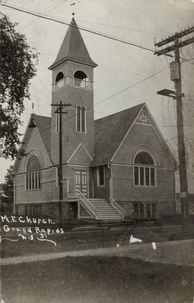 View of the M.E. Church. There are steps up to the corner entrances. Caption reads: "M.E. Church, Grand Rapids, Wis."