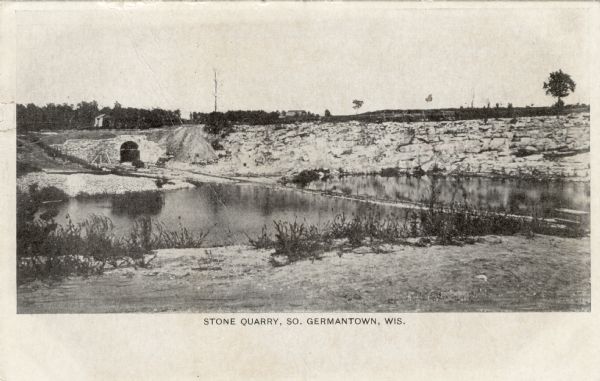 View of a stone quarry next to a river. Tracks are leading into an arched entrance. Caption reads: "Stone Quarry, So. Germantown, Wis."